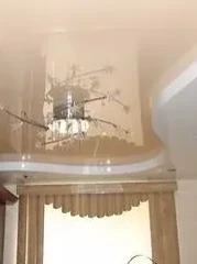 Глянцевый фигурный натяжной потолок с оригинальной люстрой и светильниками по периметру.